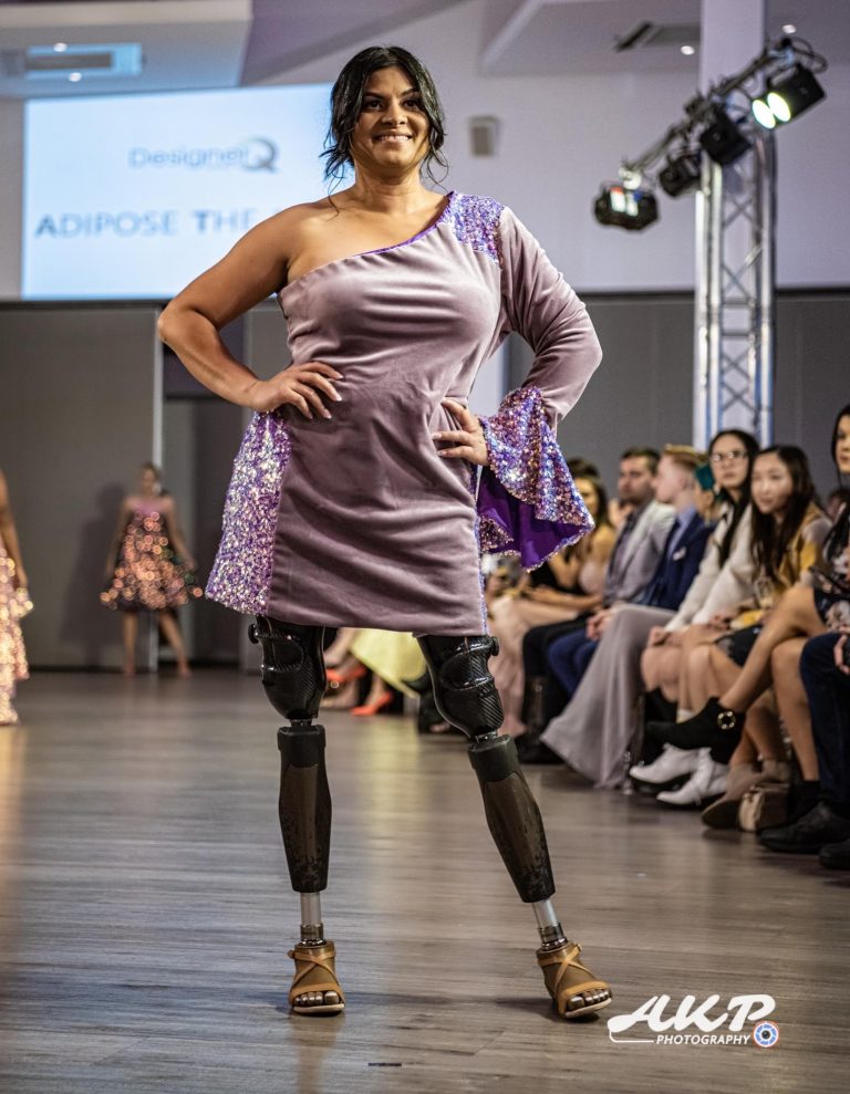Sara Shams wearing a sparkly off one shoulder purple dress posing on the runway